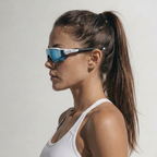 A woman in profile wearing TEROVIK APEX sport sunglasses with a white frame and blue mirrored lenses, paired with a white sports bra against a plain light gray background.